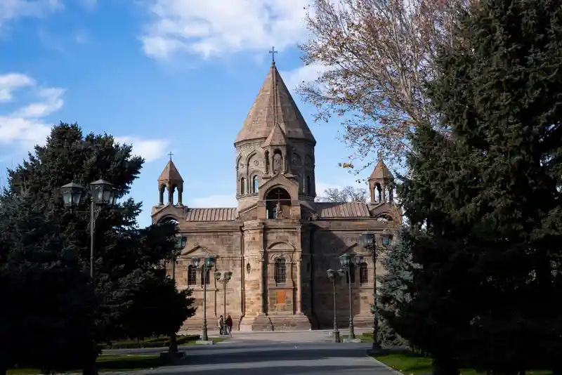 It shows the Mother Cathedral of Echmiadzin with two very large trees on either side.