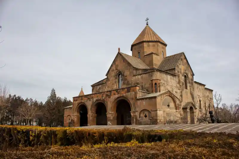 The image shows Saint Gayane Church in Armenia with a basilica shape and a central dome on a cloudy day.