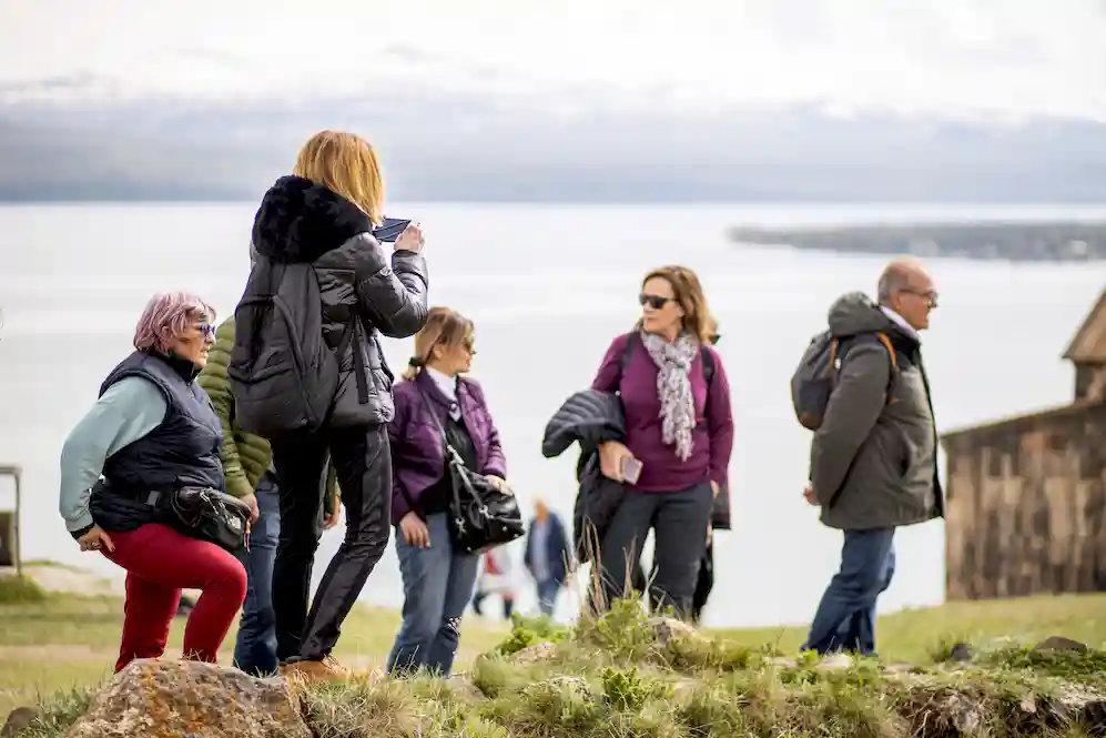 Several tourists on the shores of Lake Seván and one of them taking a photo.
